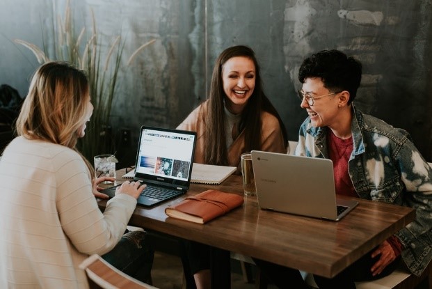 Three people at a table with laptops and notebooks laughing