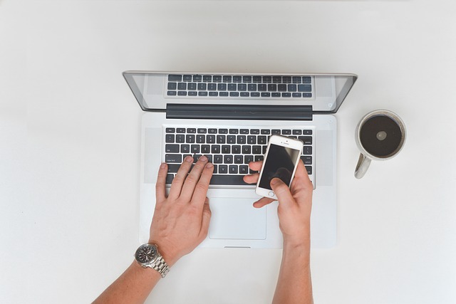 A person hands with laptop holding a phone with a coffee on the table